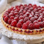 Raspberry tart topped with chocolate drizzle and fresh raspberries