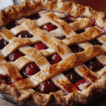 Close-up of a freshly baked cherry pie with a golden-brown, flaky crust and visible juicy cherry filling.