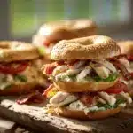 Chicken Bacon Ranch Bagels stacked on a rustic wooden board with crispy bacon and ranch