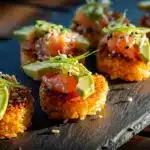 Golden Crispy Rice Salmon Bites topped with spicy salmon and avocado on dark slate