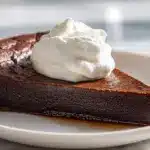 A slice of chocolate impossible pie with whipped cream on a ceramic plate