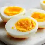A bowl of perfect hard boiled eggs with smooth whites and bright yellow yolks on a wooden board.